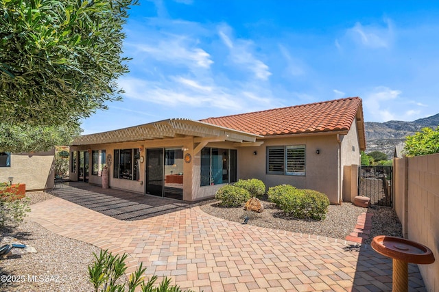 rear view of house featuring stucco siding, a mountain view, a patio area, a tiled roof, and fence