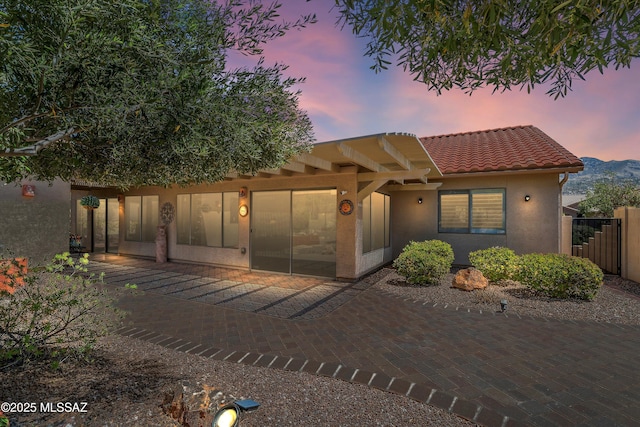 view of front of house featuring a tiled roof, fence, a patio area, and stucco siding