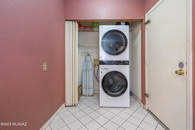 laundry room featuring a textured wall, light tile patterned flooring, stacked washer and dryer, and laundry area