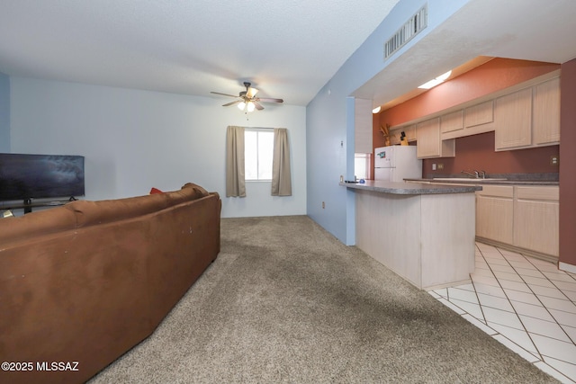 kitchen featuring a peninsula, open floor plan, visible vents, freestanding refrigerator, and ceiling fan