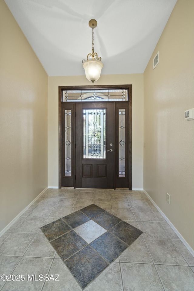 tiled entryway with visible vents, baseboards, and lofted ceiling