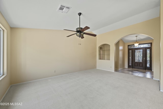 unfurnished living room featuring ceiling fan, arched walkways, visible vents, carpet flooring, and baseboards