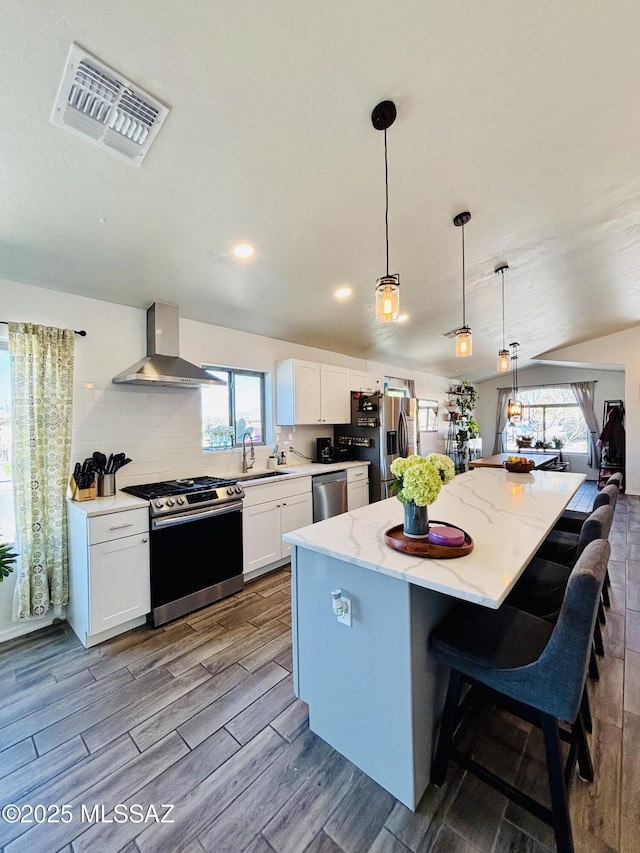 8332 S Otis Dr, Tucson, AZ 85747 - kitchen with lofted ceiling, stainless steel appliances, visible vents, wall chimney exhaust hood, and light wood-style flooring