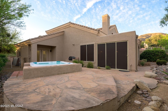 rear view of property featuring a chimney, a tile roof, a patio area, and stucco siding
