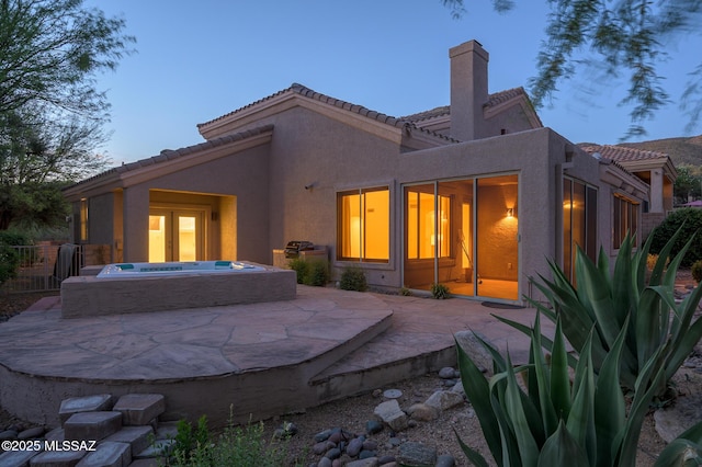 rear view of house with stucco siding, a patio area, and a tile roof