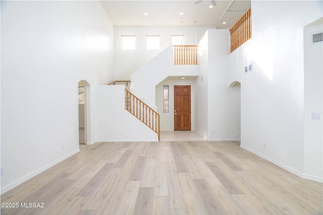 interior space featuring a high ceiling, arched walkways, wood finished floors, visible vents, and stairway