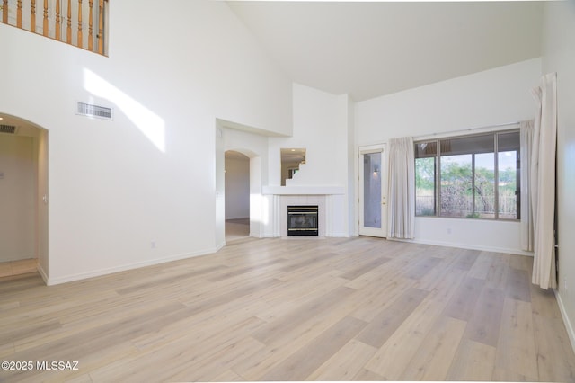 unfurnished living room featuring visible vents, arched walkways, light wood finished floors, and high vaulted ceiling