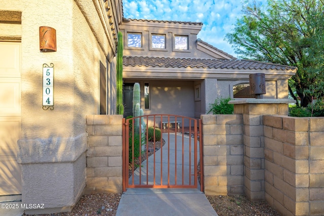 property entrance with a tile roof, a gate, and stucco siding