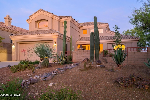 mediterranean / spanish home featuring fence, stucco siding, a tiled roof, concrete driveway, and an attached garage