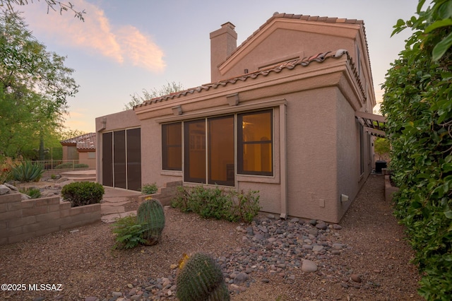 back of house at dusk with a chimney and stucco siding