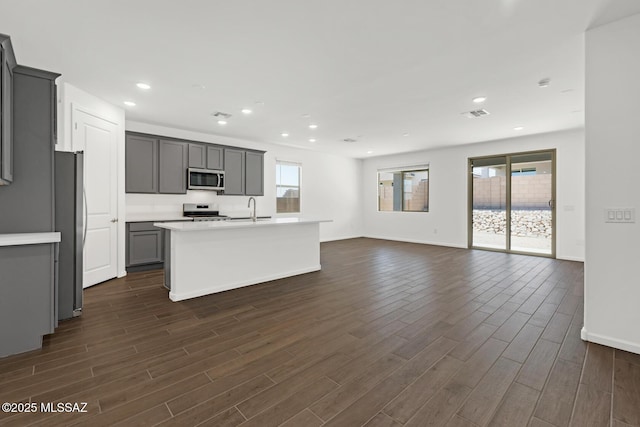 kitchen featuring open floor plan, gray cabinetry, dark wood finished floors, and stainless steel appliances