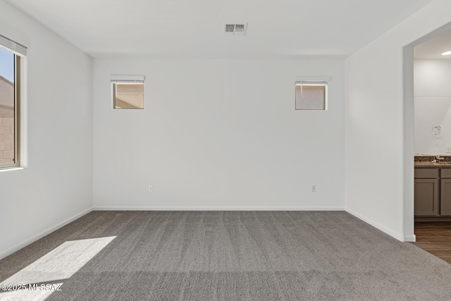 unfurnished room with baseboards, dark colored carpet, and visible vents