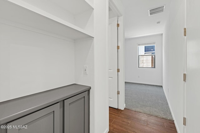 hall with visible vents, baseboards, and dark wood-style floors