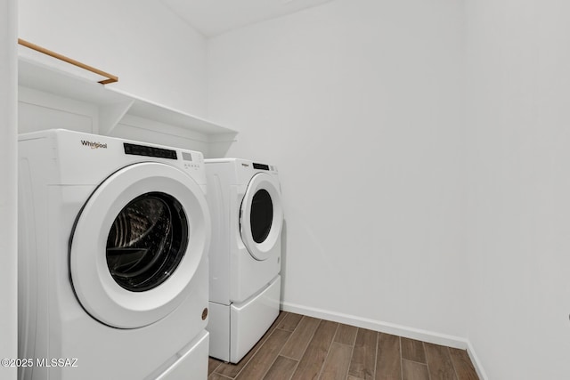 washroom featuring washing machine and dryer, laundry area, baseboards, and wood finished floors