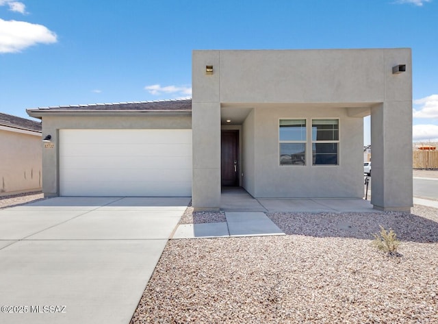 pueblo-style home with an attached garage, driveway, and stucco siding