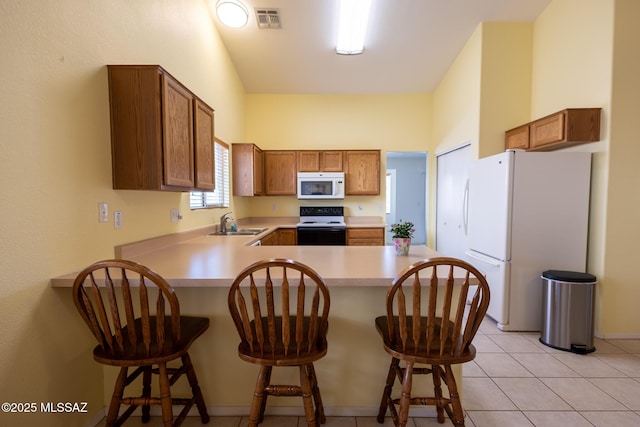 10532 E Malta St, Tucson, AZ 85747 - kitchen with white appliances, a peninsula, light countertops, a breakfast bar, and brown cabinets