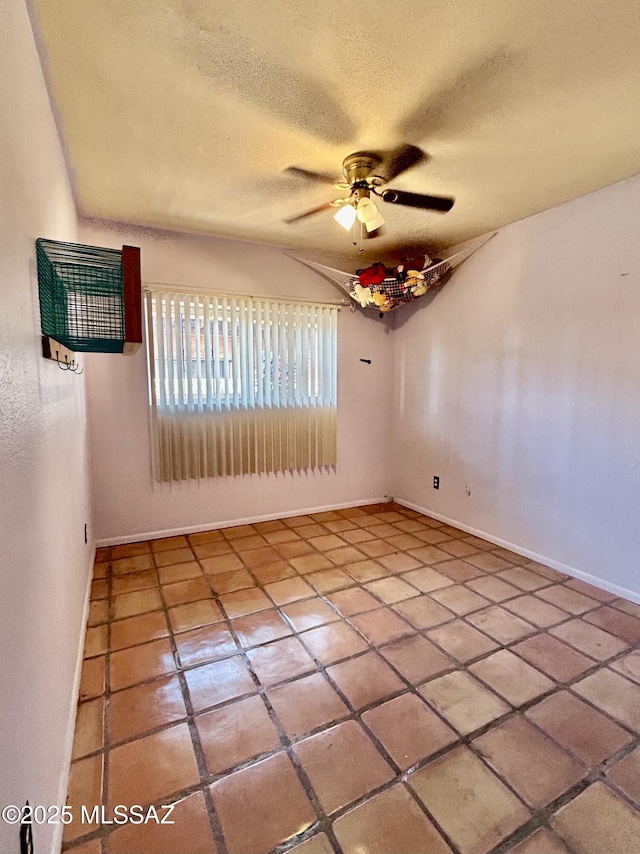 empty room featuring tile patterned flooring, a ceiling fan, a textured ceiling, and baseboards