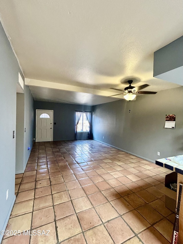 interior space with light tile patterned floors, a ceiling fan, a textured ceiling, and baseboards