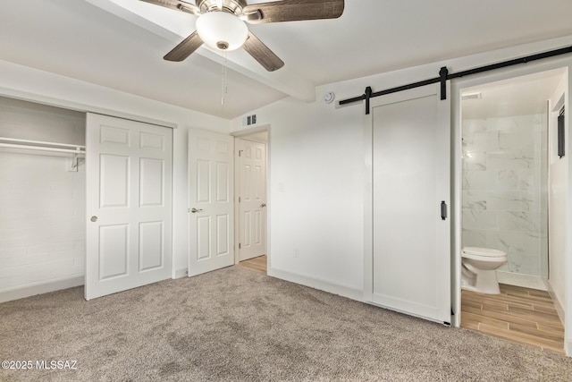 unfurnished bedroom featuring visible vents, a barn door, carpet floors, beamed ceiling, and connected bathroom