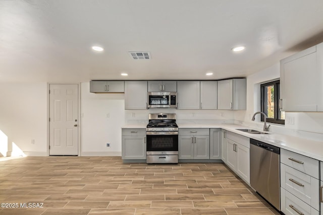 kitchen featuring light wood-type flooring, visible vents, gray cabinets, appliances with stainless steel finishes, and a sink