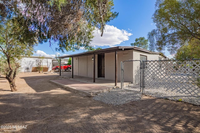 rear view of property with a patio area, concrete block siding, fence, and a gate