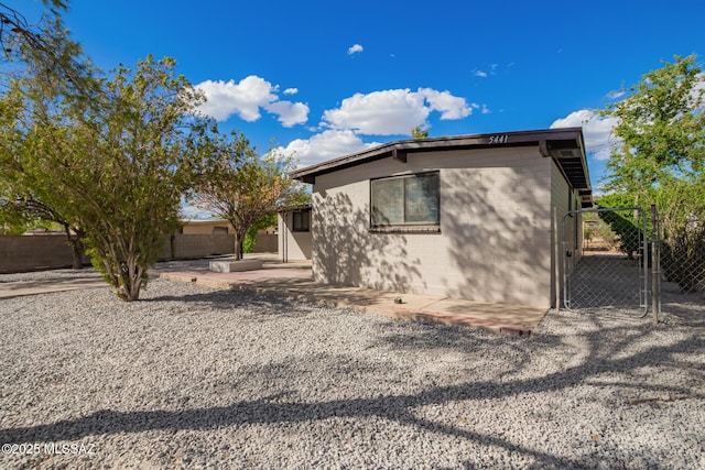 exterior space with a patio area, concrete block siding, fence, and a gate