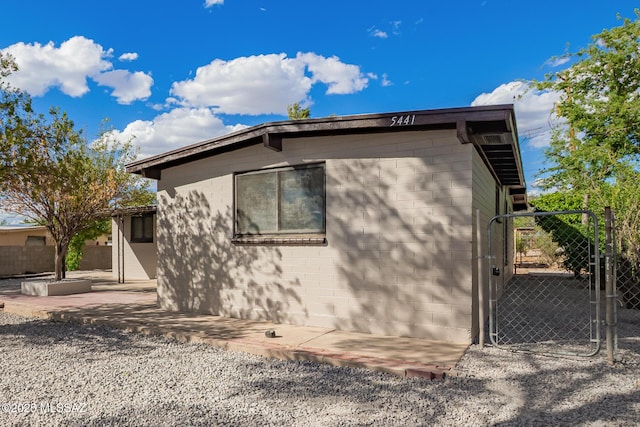 view of property exterior with a patio area, concrete block siding, fence, and a gate