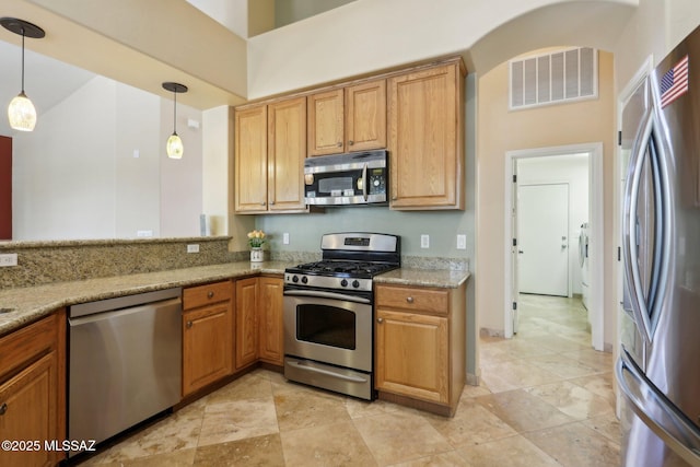 kitchen with light stone countertops, decorative light fixtures, visible vents, brown cabinetry, and appliances with stainless steel finishes