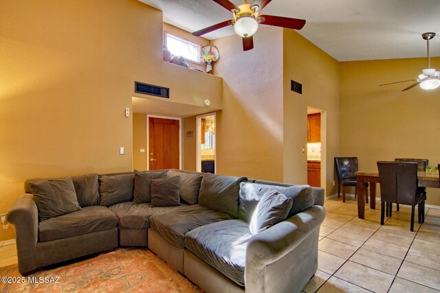 living area featuring light tile patterned flooring, visible vents, baseboards, a towering ceiling, and a ceiling fan