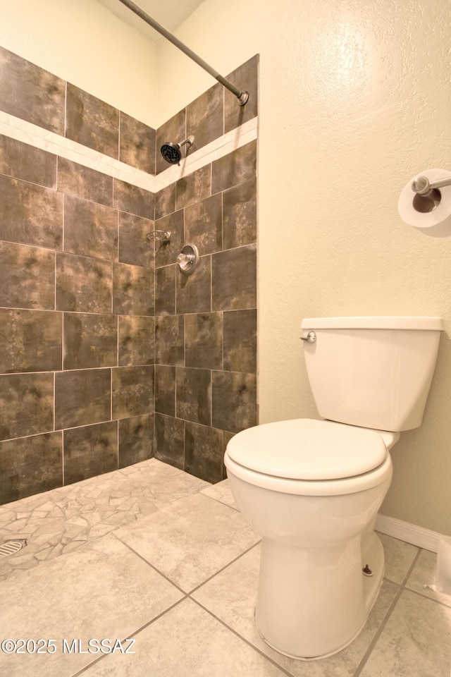 full bathroom featuring baseboards, toilet, tile patterned floors, and tiled shower