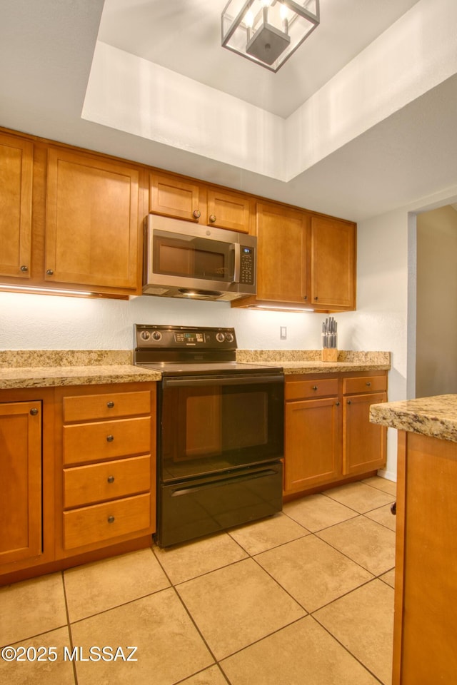 kitchen with a tray ceiling, brown cabinetry, black / electric stove, and stainless steel microwave