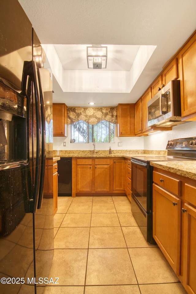 kitchen with light tile patterned floors, a tray ceiling, black appliances, and brown cabinets
