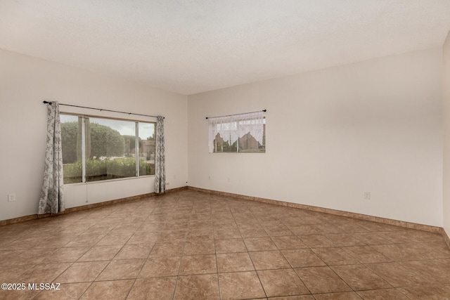 empty room featuring baseboards, a textured ceiling, and light tile patterned floors