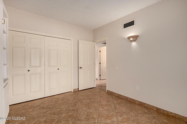 unfurnished bedroom with a closet, a textured ceiling, visible vents, baseboards, and tile patterned floors