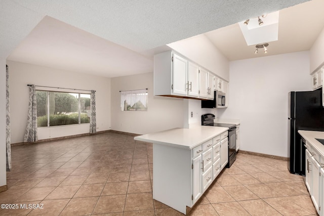 kitchen featuring light countertops, light tile patterned floors, a skylight, white cabinets, and black appliances