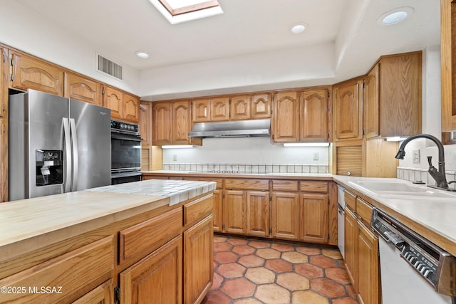 kitchen featuring dobule oven black, a sink, visible vents, dishwasher, and stainless steel fridge