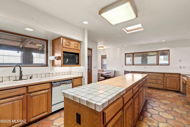 kitchen featuring tile counters, a kitchen island, dishwasher, a sink, and black microwave