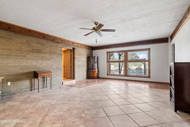 unfurnished living room featuring a ceiling fan, a textured ceiling, light tile patterned flooring, and brick wall