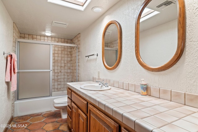 bathroom with a textured wall, vanity, visible vents, and a skylight