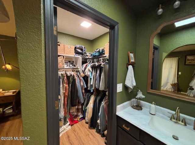 bathroom featuring a textured wall, a spacious closet, vanity, and wood finished floors