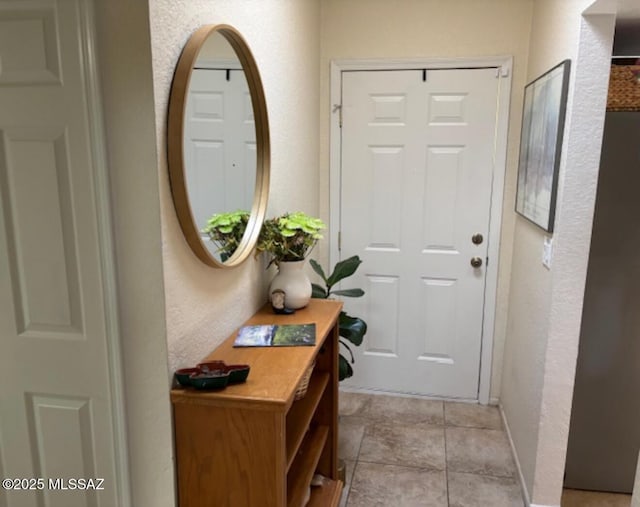 doorway to outside with a textured wall and baseboards