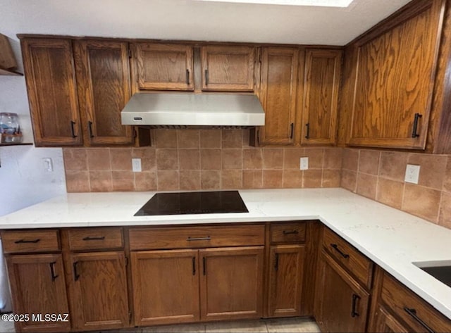 kitchen with range hood, light countertops, black electric stovetop, and backsplash