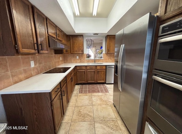 kitchen with light tile patterned flooring, under cabinet range hood, decorative backsplash, stainless steel appliances, and a sink