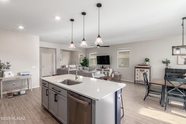 kitchen with light countertops, a sink, stainless steel dishwasher, open floor plan, and light wood-style floors