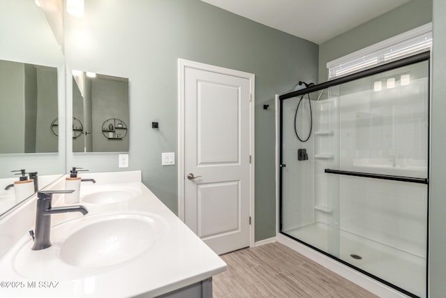 bathroom with a shower stall, double vanity, wood finished floors, and a sink