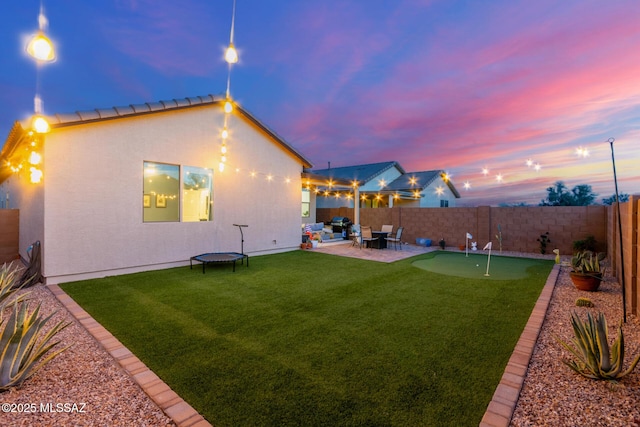 rear view of house with stucco siding, a fenced backyard, a lawn, and a patio area