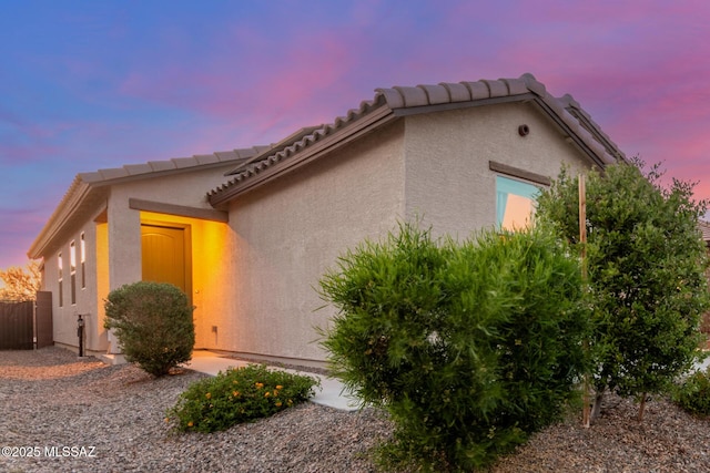 view of property exterior with a tile roof, stucco siding, and fence