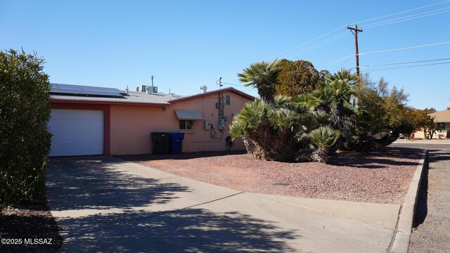 view of front of property featuring roof mounted solar panels, an attached garage, concrete driveway, stucco siding, and cooling unit