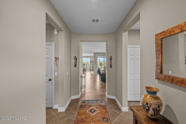 hall featuring baseboards, dark tile patterned flooring, and visible vents