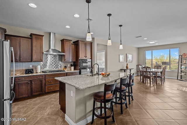 kitchen featuring wall chimney range hood, light tile patterned flooring, tasteful backsplash, and appliances with stainless steel finishes